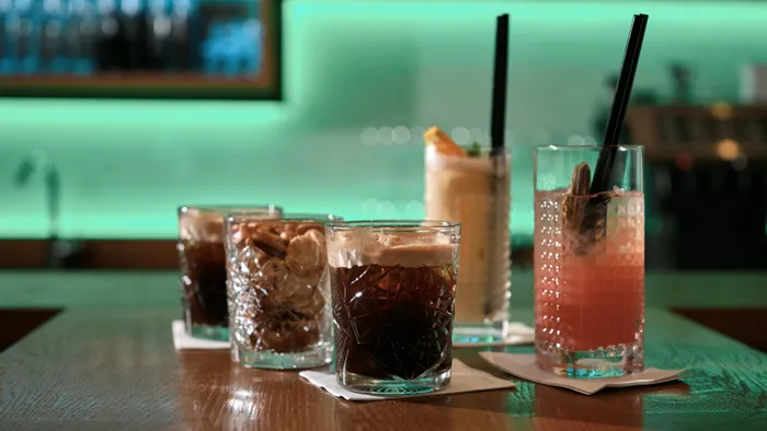 Verschiedene Cocktails in strukturierten Gläsern auf Bartheke mit grünem Neonlicht